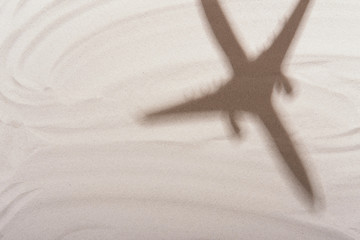 Fototapeta na wymiar Shadow of plane or airplane on white sand background. Flat lay design. Travel, vacation concept