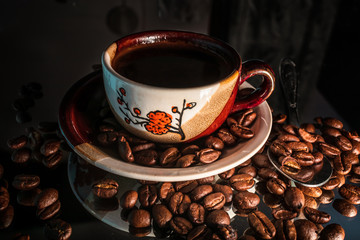 Small cup of coffee and coffee beans with reflection on shiny black background