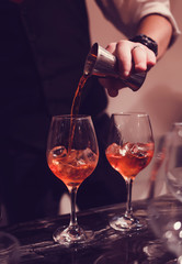 the bartender pours sweet syrup into a glass with ice makes an alcoholic drink on the bar