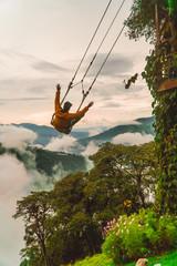 Man on giant swing Ecuador. Tourist having fun swinging on Giant Swing in Casa del Arbol attraction. View of green mountains and trees in background. Wooden Treehouse. Shot in Banos, Ecuador