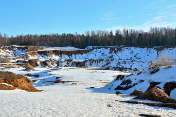 Fototapeta premium View from the mountain to the red sand in the snow of a small canyon in the Minsk region, Radoshkovichi, the village of Praleski, mining quarry.