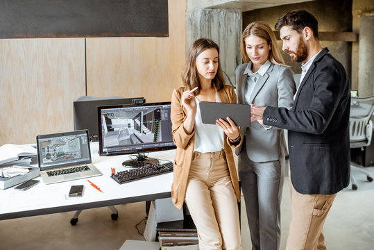 Small group of creative office employees working with digital tablet, standing together in the modern office of architectural firm