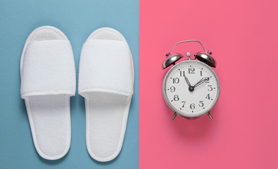 White hotel sleeping slippers and alarm clock on colored background. Time to sleep. Top view