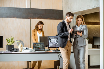 Strictly dressed office employees working with digital tablet and computers at the architectural...