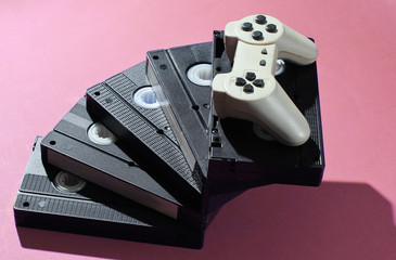 Gamepad on stack of retro video cassettes. Minimalism studio shot on pink background