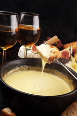 Gourmet Swiss fondue dinner on a winter evening with assorted cheeses on a board alongside a heated pot of cheese fondue with two forks dipping