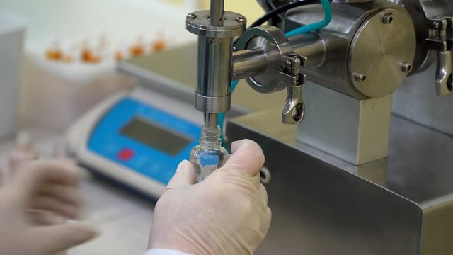 Semi-automatic filling of vials with the cosmetics cream at the factory.