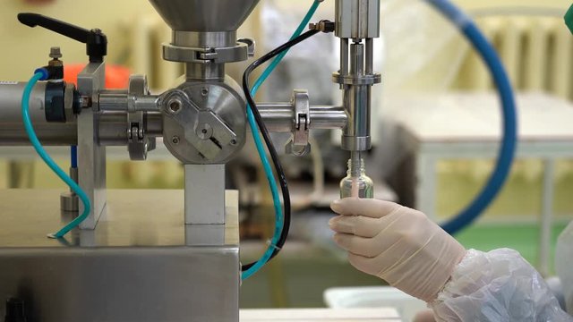 Semi-automatic filling of vials with the cosmetics cream at the factory.