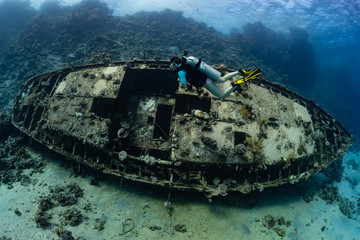 woman diver visiting an underwater wreck of a metal sailboat on a reef in the Rea Sea, Egypt