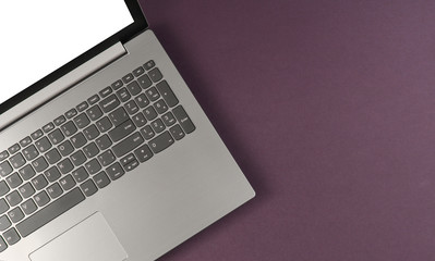Fragment of laptop with a white screen on purple background. Top view