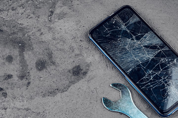 Crashed smartphone with repairing tools on grey background