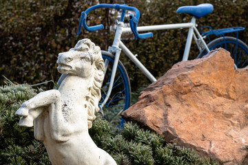 A decorative statue of a horse standing on its hind legs in a garden with a blue-stained bystander in the background