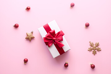 christmas gift box with red ribbon on a pastel pink background with red christmas tree toys, golden stars and cones. Holidays, New Year 2020 present concept. Trendy colors,Top view, flat lay.