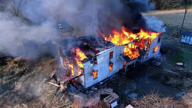 Sad Remains Of House Completely Destroyed In A Fire, Firefighters In The Background Prevent Spreading Of Fire, Controlled Burn Down