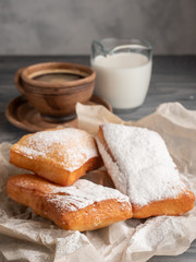 Beignet sprinkled with icing sugar on a wooden table with coffee and milk.