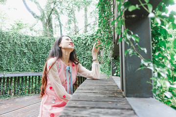 Young beautiful asian woman in pink dress relaxing in wooden hall with plant