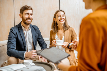 Young couple talking with a sales manager or real estate agent, offering some products with a...