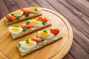 healthy crispbread open sandwiches with boiled eggs and fresh tomatoes cream cheese on round cutting board