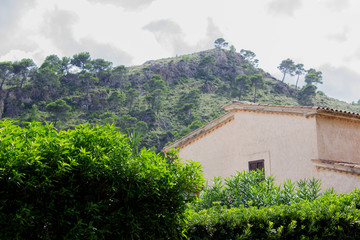 View of House with Rich Foliage in Foreground and Mountains in Background at the City of Cala Sant Vicent, Mallorca, Spain 2018 - 304984117
