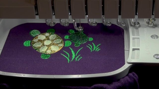  work of the embroidery machine with the green  thread  when performing work on the automated production of a colored design grass and turtle  on the purple background