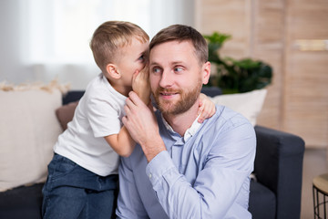 little son whispering a secret at ear to his daddy