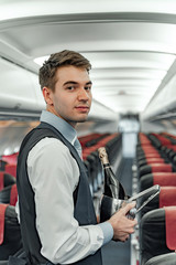 Young flight attendant with champagne bottle in cabin