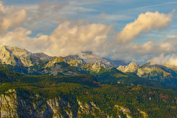 Obraz premium High perspective view of mountains during sunset. Some mountain peaks are covered with thick white clouds which backlit by the sun. Concept of landscape and nature. Triglav National Park, Sloenia