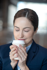 Dark-haired businesswoman smelling coffee while enjoying drink in the morning