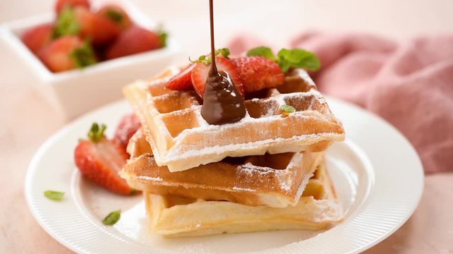 Chocolate sauce pouring on belgian waffles. Sweet breakfast food, unhealthy eating. Sugar food