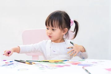 Adorable asian little girl is concentrate playing by color painting on hands and on white paper, concept of art education activity for kid learning.