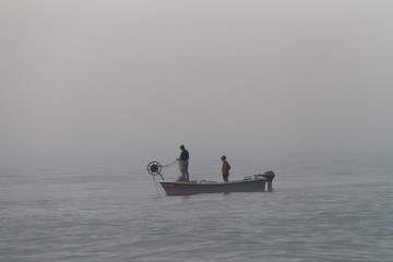 Naklejka premium Fishermen on the boat in foggy morning, Long Beach in Ulcinj in Montenegro