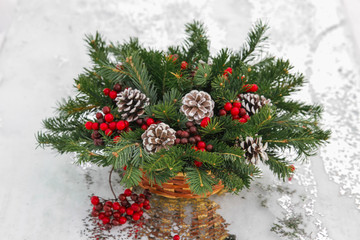 Closeup New Year wicker basket with snow covered spruce evergreen branches, cones and red berries.