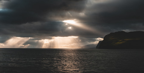 Naklejka na ściany i meble Beautiful rays of sun breaking through the clouds in Sandoy and Hestur ferry travel, Faroe Islands