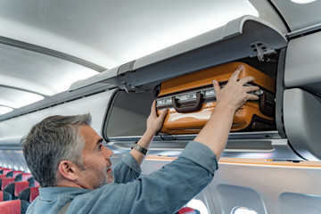 Smiling man putting his luggage on shelf in cabin