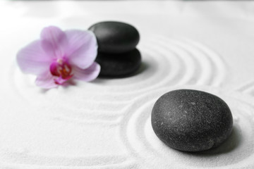 Fototapeta na wymiar Black stones and beautiful flower on sand with pattern. Zen, meditation, harmony