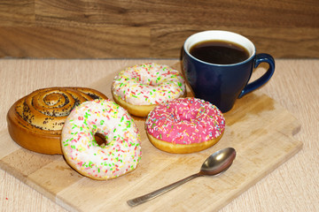 Multi-colored donuts and a bun with poppy seeds lie on a wooden table next to an empty blue cup. Top landscape with a place for text. Template for design. Spare photo.