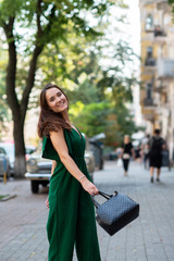 Fototapeta premium Fashion model wearing green overall posing outdoor. Young beautiful brunette caucasian woman walking summer streets. Beautiful girl, urban portrait.