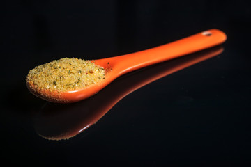 Orange ceramic spoon with mixture of spices, with reflection on shiny black background