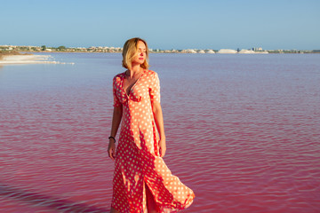 Woman wearing dotted dress walking at bang of salty pink lake with crystals of salt. Extremely salty pink lake, colored by microalgae with crystalline salt depositions in Torrevieja, Spain