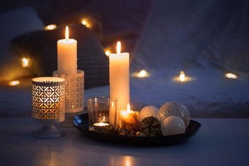 Christmas decoration   with burning candles on  white table against the background of  sofa with plaids and pillows. Cozy home and holiday concept