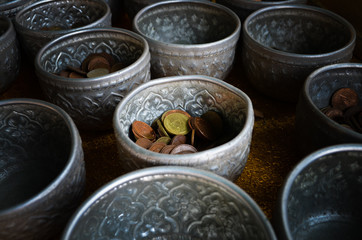 Golden, bronze and silver Thai coins separated in silver bowls for Thai traditional donation at Buddhist temple in Thailand. Coins background texture.
