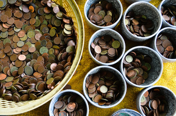 Golden, bronze and silver Thai coins in plastic basket and silver bowls for donation at Buddhist temple in Thailand. Coins background texture.