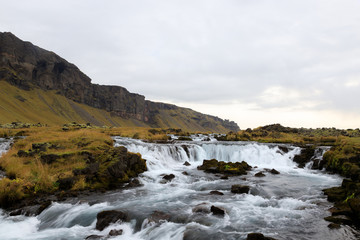 Obraz premium Panoramic summer view of small waterfall near Bjodvegur road. Wonderful sunrise on Iceland, Vik location. Beauty of nature concept background..