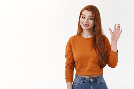Friendly cheerful good-looking girl redhead long hair smiling joyfully raise hand waving hello hi greeting gesture grinning pleasant introduce herself welcoming guest, stand white background goodbye