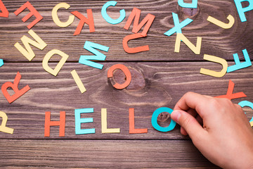 Children`s hands make up the word "hello" from colored carved cardboard letters on a wooden background. Top view