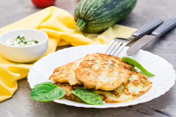 Vegetable fried fritters from zucchini and basil leaves on a plate and cutlery on the table
