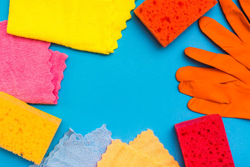 Colored sponges for washing dishes, microfiber rags and rubber gloves laid out with a frame on a blue background. Cleaning Tools Concept. Copy space