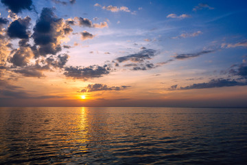 Amazing summer sunset view on the beach. Beautiful blazing sunset landscape at black sea and orange sky above it with awesome sun golden reflection on calm waves as a background.