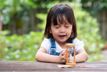 Adorable asian little girl is looking and observing the flow of sand inside the hourglass, concept of learning activity for kid.