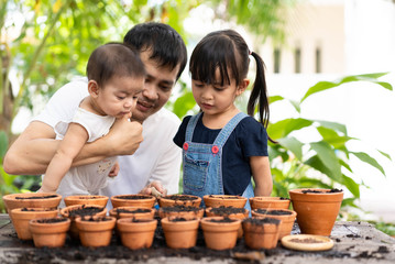 Asian father teaching his child how to planting step by step in the garden outside the house,...